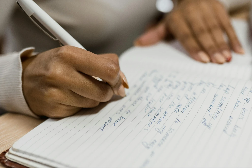 Mão feminina de pessoa de pele negra com caneta escrevendo em caderno