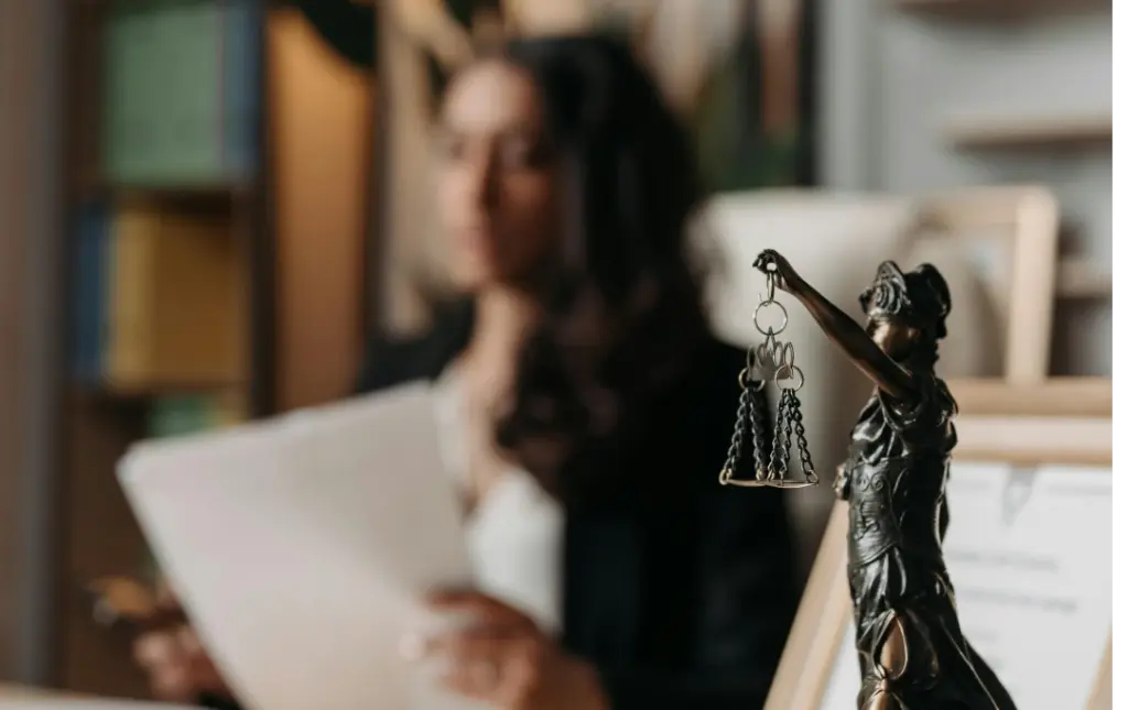 Estátua da justiça em mesa de escritório com mulher trabalhando ao fundo
