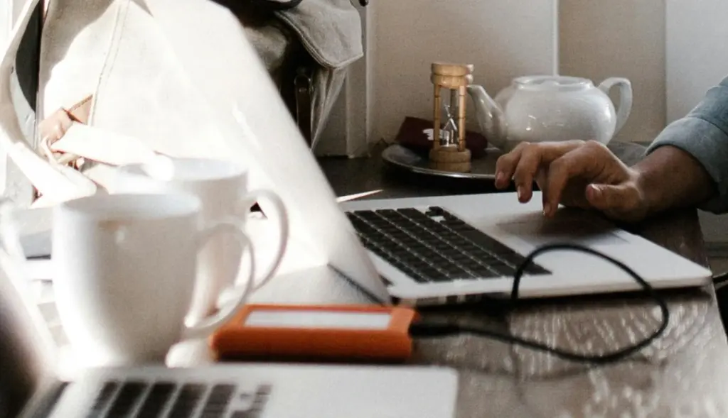 Mulher mexendo em notebook e segurando xícara de café, computador com bateria carregando
