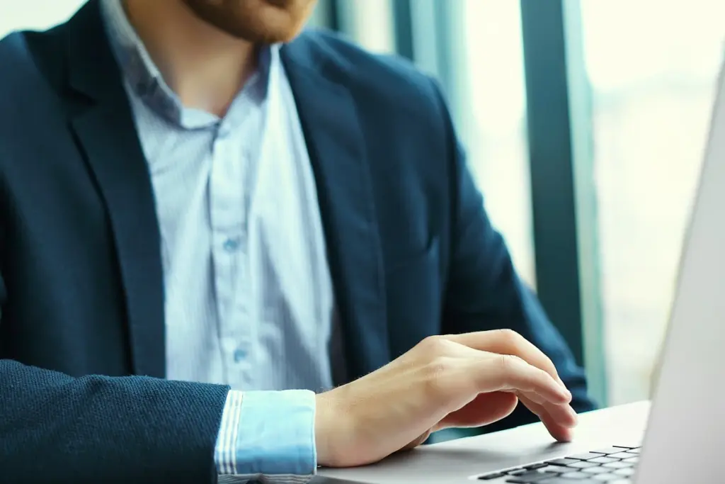 Homem de roupa social mexendo em notebook sobre a mesa