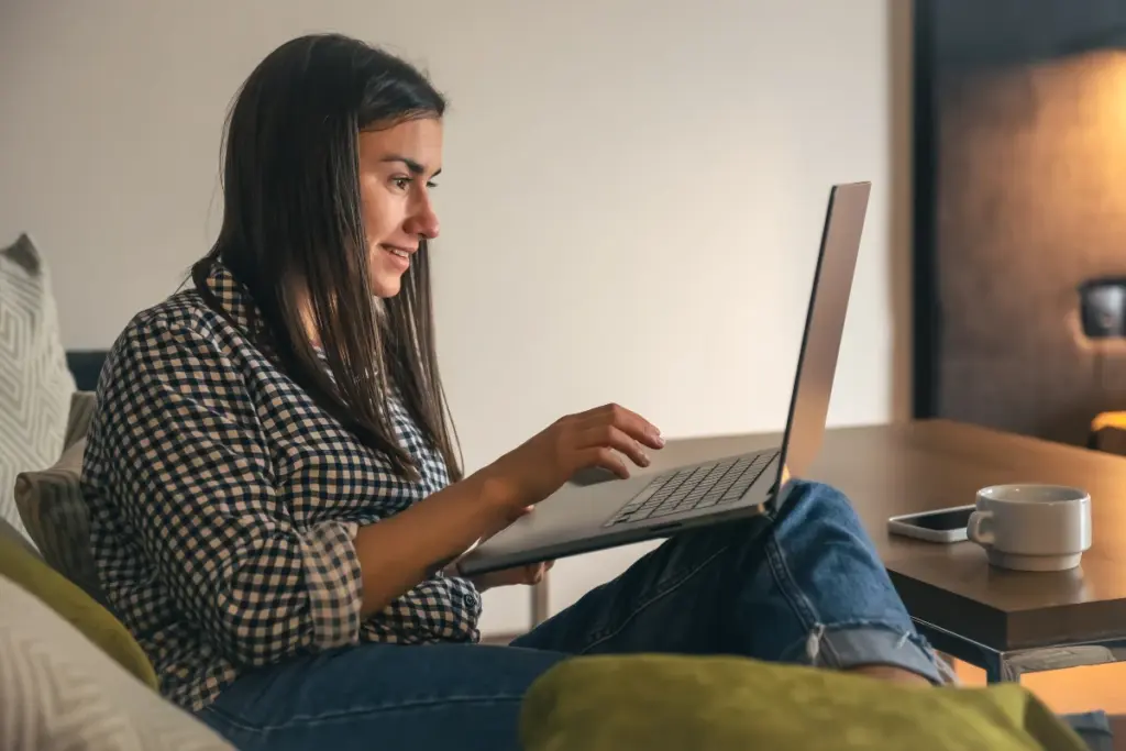 Mulher mexendo em notebook em casa sentada em sofá