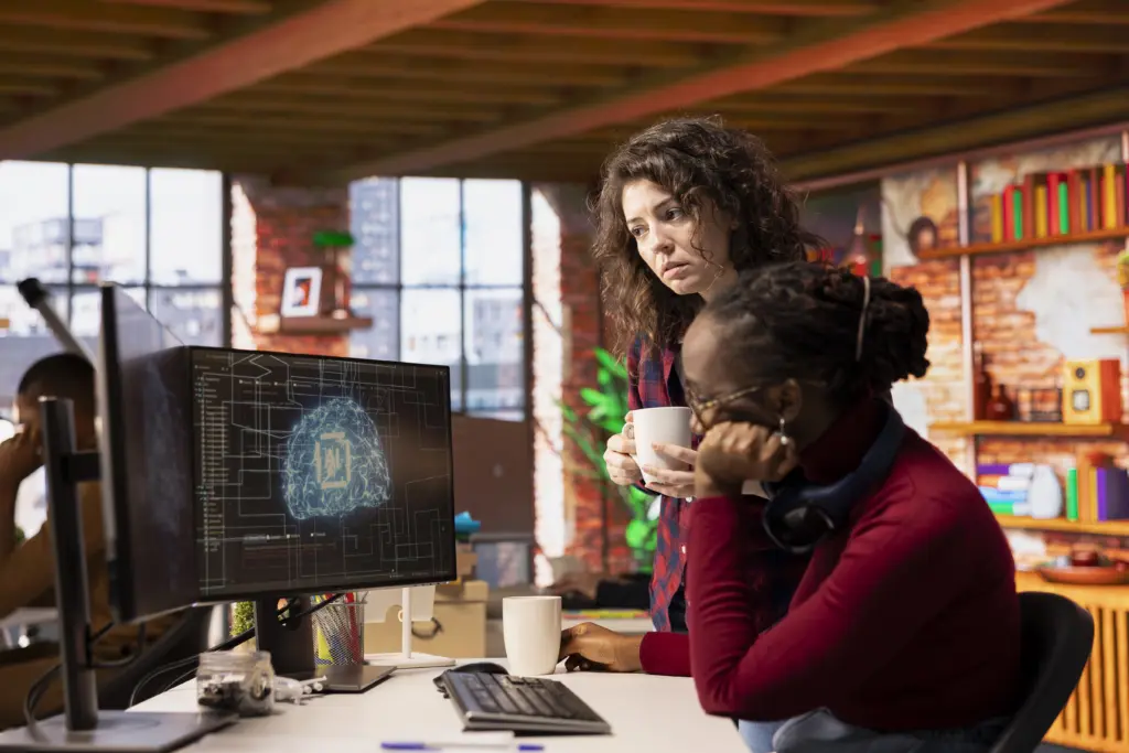 Duas mulheres ao computador, conversando sobre IA